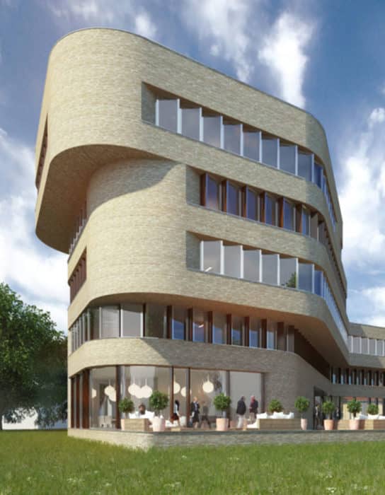 Ein modernes, geschwungenes Gebäude mit großen Fenstern und einer Backsteinfassade. Menschen sitzen draußen an Tischen auf einer Terrasse mit Topfpflanzen. Das Gebäude ist von Gras und einem Baum umgeben, der Himmel ist teilweise bewölkt.