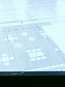 Eine Nahaufnahme eines technischen Grundrisses oder einer architektonischen Blaupause mit verschiedenen Symbolen, Tabellen und detaillierten Linien, die auf einem beleuchteten Zeichentisch angezeigt werden.
