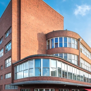 Ein modernes Backsteingebäude mit abgerundeten Ecken und großen Fenstern, die den blauen Himmel reflektieren, aus einem niedrigen Winkel vor dem Hintergrund eines klaren Himmels und Sonnenlichts fotografiert.