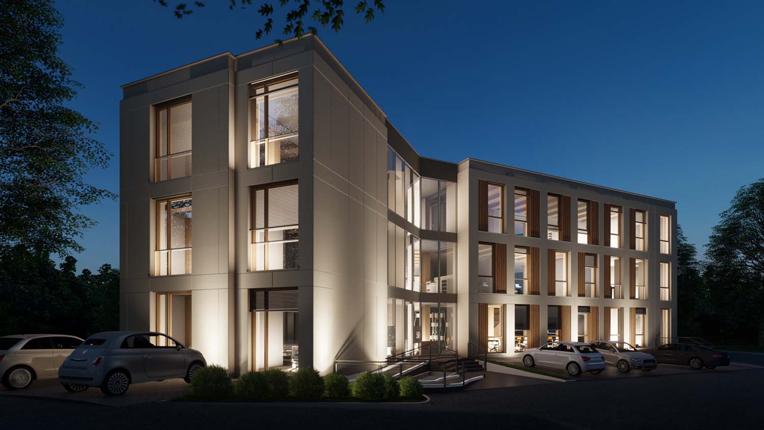 Ein modernes dreistöckiges Bürogebäude mit großen Fenstern ist nachts beleuchtet. Mehrere Autos parken draußen, und sanftes Licht unterstreicht die zeitgenössische Architektur des Gebäudes. Bäume und Grünflächen umgeben das Gebäude.